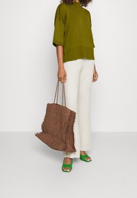 Olivově zelený žebrovaný pletený top, krémové kalhoty s širokými nohavicemi, hnědá tkaná taška a jasně zelené sandály na otevřenou špičku s texturovanými popruhy.