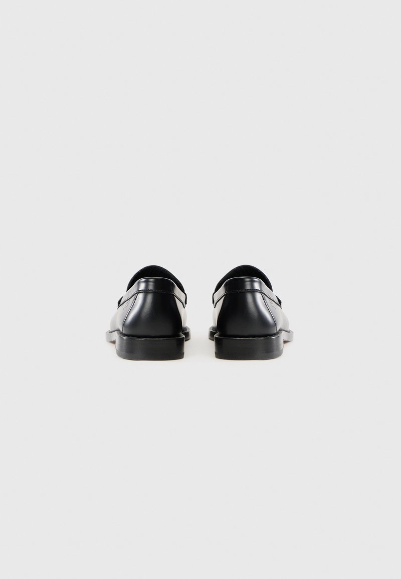 Zwarte lederen schoenen met een gladde textuur, ronde neus en een lage hak, met een minimaal ontwerp zonder zichtbare hardware of accenten.