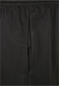 Shorts de sport noirs en tissu maillé respirant. Dotés d'une taille élastique et de poches latérales. La texture est légèrement côtelée.