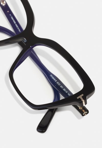 Montura de gafas de plástico negro con lentes cuadrados, acentuada por un logo dorado, con una patilla texturizada en púrpura.