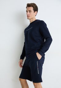 Granatowy komplet bluzy i szortów, wykonany z miękkiego materiału. Bluza ma haftowane logo; szorty mają nadrukowaną markę z boku.