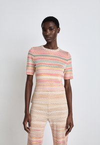 Strickoberteil und Hosen-Set mit einem mehrfarbigen Zickzack-Muster in den Farbtönen Pink, Grün und Beige. Kurze Ärmel, runder Halsausschnitt, figurbetonte Passform.