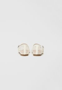 Lace-back flat shoes in cream with a mesh design, round toe, and a small heel, featuring a silver-tone buckle detail.