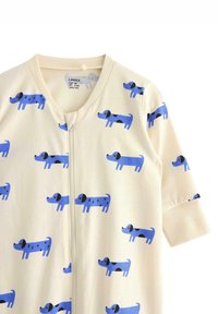 Lichtbeige jumpsuit met herhaalde blauwe cartoonhonden met zwarte accenten, lange mouwen en een rits aan de voorkant. Van zachte katoen.