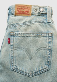 Φωτεινά γαλάζια τζιν denim με ξεθωριασμένη υφή, που διαθέτουν καφέ δερμάτινο έμπλαστρο, ασημί κουμπί και κόκκινη ετικέτα Levi's στην πίσω τσέπη.