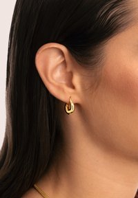 Los pendientes de aro de oro presentan una forma elegante de lágrima con una superficie pulida. Están sujetos a un simple gancho de oro.