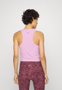 T-shirt atlético rosa claro com um design de costas nadador. Usado sobre leggings burgundy estampadas com um padrão de animal escuro.