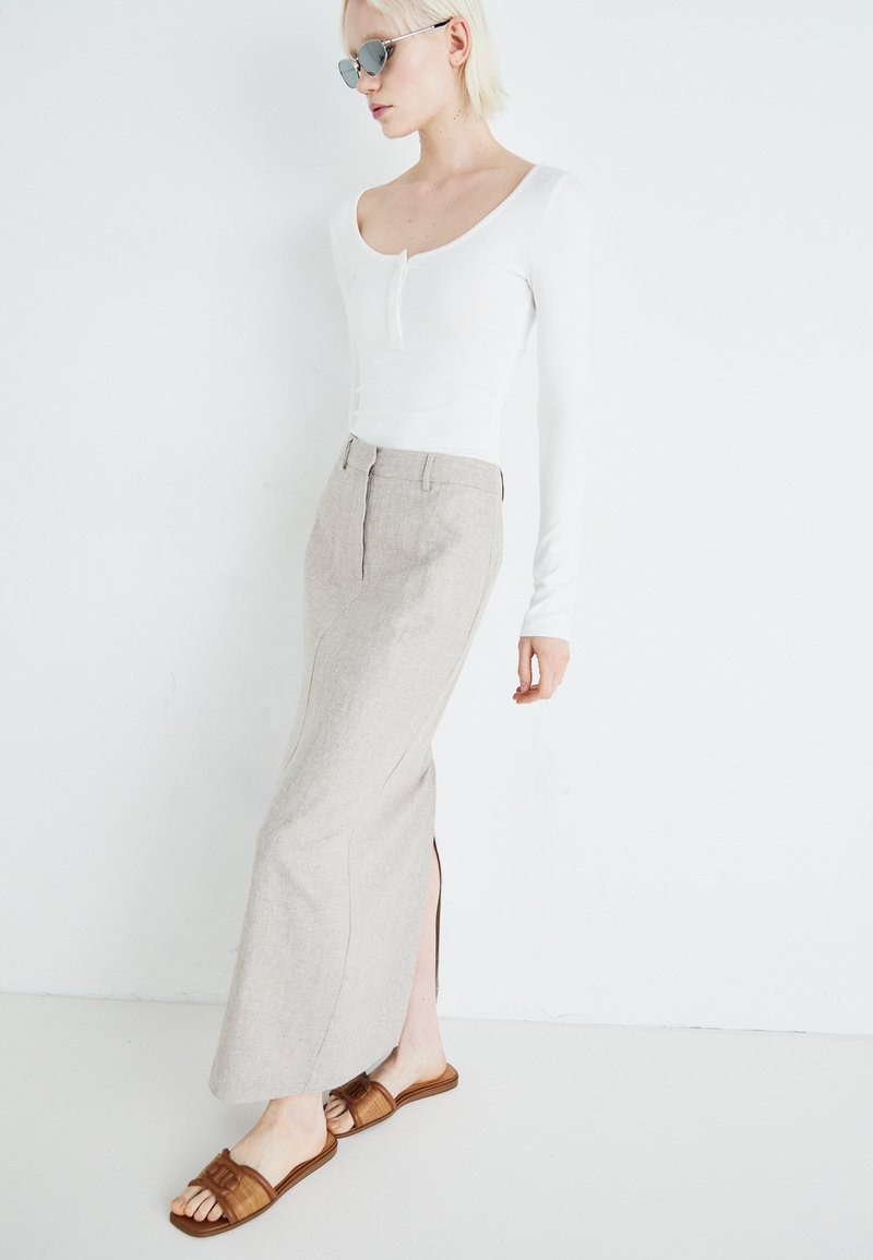 Witte lange mouw top met een ronde hals, gecombineerd met een beige linnen maxi rok met een zijsplit. Bruine slippers met een banddetail.