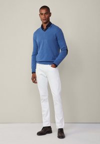 Sininen villapaita, jossa on v-pääntie, valkoiset farkut ja tummat kengät. Villapaita on sileäpintainen; farkut ovat istuvia. Kaiken kaikkiaan rento asu.