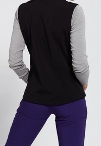 Czarna bezrękawnikowa kamizelka na szarej, długiej koszuli, zestawiona z fioletowymi spodniami. Gładki materiał o dopasowanym kroju i minimalnych detalach.