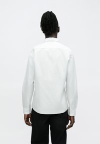 Camisa de manga larga con rayas blancas, cuello clásico, puños abotonados y dobladillo recto. La tela es suave con una textura sutil.