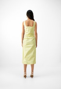 Robe midi jaune élégante avec un col carré et une coupe ajustée, présentant une texture lisse et un léger froncé à l'arrière.