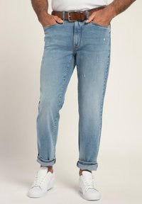 Jeans in denim azzurro chiaro con dettagli strappati, taglio dritto e orli arrotolati, abbinati a sneakers bianche e una cintura in pelle marrone.