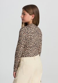 Długi rękaw top z wzorem w panterkę na beżowym tle, w połączeniu z jasnymi spodniami cargo z tylnymi kieszeniami.