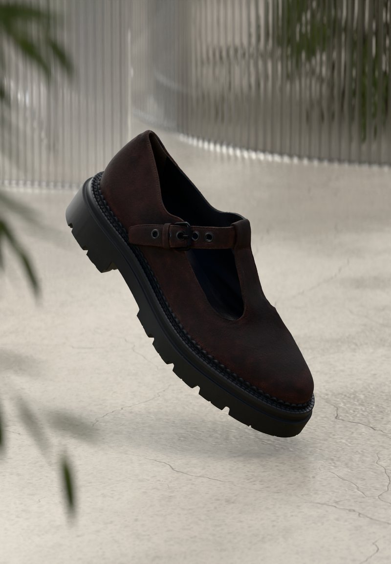 Chaussure en cuir marron foncé avec un design découpé, une sangle à boucle ajustable et une semelle en caoutchouc noir épais avec une texture de semelle.
