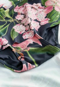 Blommig baddräkt med rosa blommor på en marin bakgrund, tillverkad av mjukt tyg; inkluderar mörka sömmar och ett distinkt lövdesign.