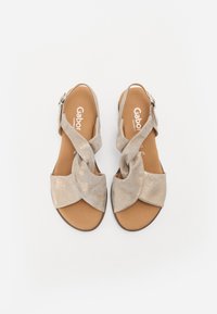 Sandales beiges avec des lanières croisées en un matériau doux et texturé. Elles disposent d'une semelle intérieure marron et d'une sangle de cheville réglable avec des éléments en métal argenté.