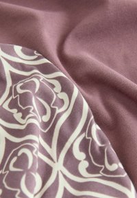 Bavlněná látka v mauve a bílé barvě se vzorovaným designem s květinovými tvary. Hladký povrch s jemným leskem a splývavostí.