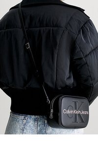 Borsa a tracolla nera dal design rettangolare elegante. Realizzata in pelle, presenta un logo impresso sulla parte anteriore e una chiusura con zip.