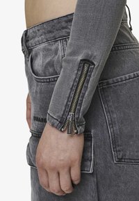 Gray denim jacket featuring a zippered sleeve detail and subtle worn texture. The garment has a fitted design with visible stitching.