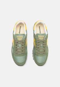 Green and yellow Saucony Shadow sneakers with mesh and suede materials, lace-up design, padded collar, and logo on tongue and heel.