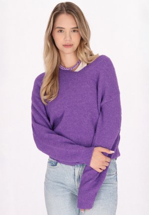 Lilla strikket sweater med afslappet pasform og v-hals, parret med lyseblå jeans. Stoffet er blødt og tekstureret, velegnet til afslappet brug.
