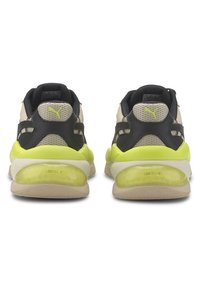 Sportovní boty s béžovým a černým svrškem, který má texturovanou síťovinu a jasně žluté akcenty, vybavené průhlednou polstrovanou podrážkou.