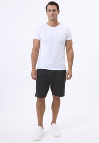 Hvid crewneck t-shirt kombineret med sorte strukturerede shorts. Modellen bærer hvide sneakers. Lige pasform og afslappet design. Minimalistisk branddetalje.