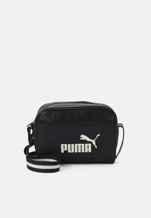 Schwarze Polyester-Crossbody-Tasche mit einem Reißverschluss, einem gestreiften Tragegurt und einem großen weißen Puma-Logo auf der Vorderseite.