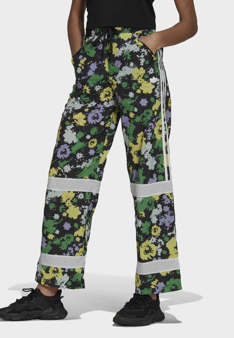 Blommig tryck joggerbyxor i svart, med gröna, lila och gula blommor. Inkluderar sidofickor och vita randiga detaljer.