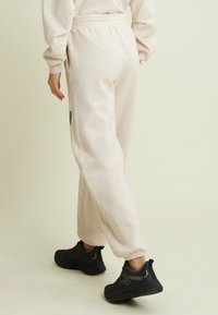 Pantalones de chándal beige claro con cintura elástica, bolsillos laterales y puños ajustados, combinados con unas zapatillas deportivas negras con marca.