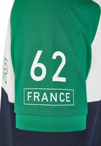 Groene en marineblauwe katoenen polo met een witte strook, groot wit "62" en "FRANKRIJK" gedrukt op de mouw, met een gestructureerde afwerking.