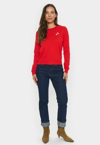 Röd stickad tröja med rund halsringning, prydd med tre vita hjärta broderier. Matchad med mörkblå jeans med uppvikta ärmar och bruna ankelstövlar.
