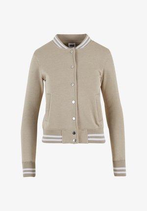 Chaqueta bomber beige con un diseño ajustado, cuello y puños acanalados con rayas blancas. Cierre con botones plateados e incluye bolsillos laterales.
