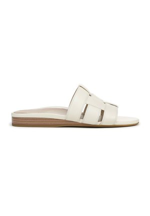 Witte instapsandaal met brede multi-strap bovenkant en platte zool met houtstructuur, zijaanzicht op een witte achtergrond.