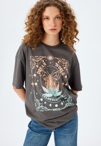 Camiseta gris de gran tamaño con un colorido diseño gráfico celestial que presenta una ilustración de una mujer, estrellas y acentos florales.