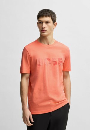 Koralfarvet kortærmet bomulds T-shirt med et mesh logo "BOSS" foran. Rund halsudskæring og afslappet pasform, parret med sorte bukser.