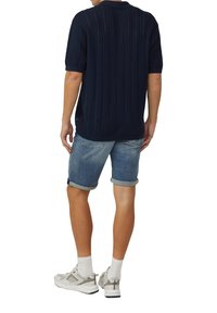 Navy gebreide polo shirt met korte mouwen, geribbelde structuur, gecombineerd met opgerolde denim shorts en lichte sportschoenen.