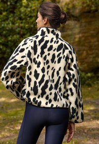 Fleece-pullov med en krämfärgad bas som har svarta leopardfläckar, krage och avslappnad passform. Kombinationen är med marinblå leggings som har en texturerad yta.