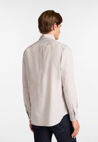 Camisa de manga larga en tejido beige claro con una textura suave, que presenta un cuello clásico y puños abotonados, mostrando un diseño liso en la parte trasera.