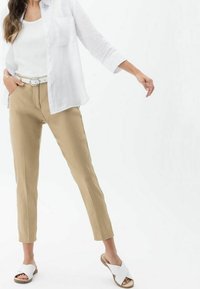 Pantaloni kaki su misura, camicia di lino bianca e sandali scivolati bianchi. L'outfit presenta una vestibilità rilassata, enfatizzando tonalità neutre e un design minimale.