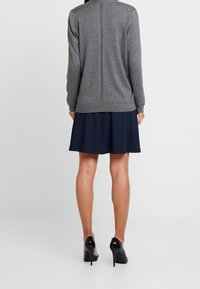 Suéter gris con una costura en la parte posterior, combinado con una falda plisada de color marino. El conjunto se completa con zapatos de tacón alto negros.