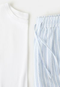 Maglietta bianca piegata accanto a pantaloni con coulisse a righe azzurro chiaro e bianco su sfondo bianco.