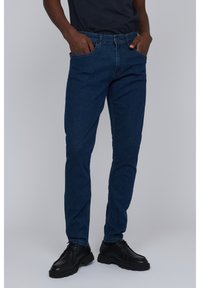 Vaqueros de mezclilla azul oscuro con un corte recto, que cuentan con bolsillos laterales, presillas para el cinturón y un diseño clásico de cinco bolsillos. Combinados con zapatos negros.