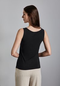 Top nero senza maniche realizzato in un tessuto morbido, con scollatura rotonda e design aderente, abbinato a pantaloni a righe beige chiaro.