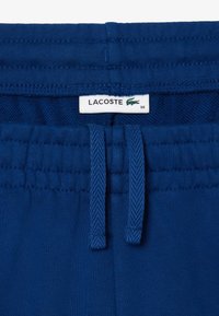 Blaue Stoffshorts mit elastischem Taillenbund und Kordelzug, strukturiertem Innenfutter und einem Lacoste-Label mit Krokodil-Logo.