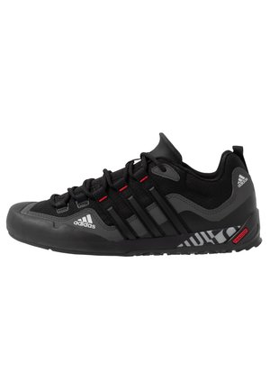 Black athletic shoe with a textured fabric upper, rubber toe cap, and red accents. Features a cushioned sole and lacing system for support.