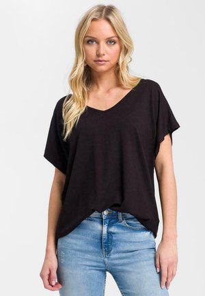 Czarny t-shirt z dekoltem w serek i krótkimi rękawami, luźny krój, wykonany z miękkiego materiału. W parze z jasnoniebieskimi, zniszczonymi dżinsami z tradycyjnym pięciokieszeniowym wzorem.