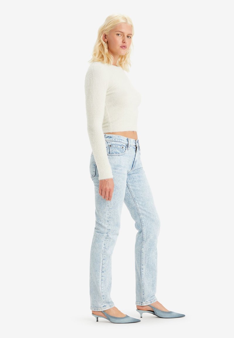 Pull court à manches longues texturé blanc, jeans taille haute bleu clair et escarpins à talons aiguille bleu clair.