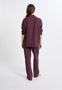 Pijamas de cuadros rojos y verdes que incluyen una camisa con botones y cuello, junto con pantalones a juego. La tela parece ligera y con un corte relajado.